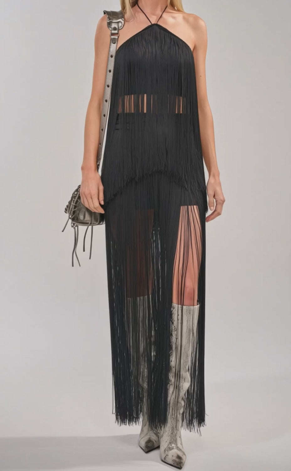 Video of woman modeling the ON THE EDGE FRINGE HALTER TOP IN BLACK styled with knee-high silver boots and a small gray shoulder bag, posing against a plain light background.