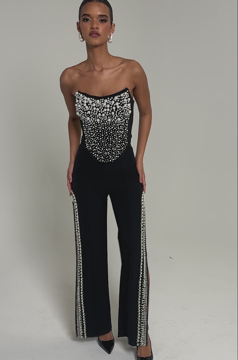 Video of woman modeling the NEVER YOURS ALL OVER PEARL CORSET, a strapless black piece featuring clusters of white faux pearl embellishments, standing against a plain light grey background.