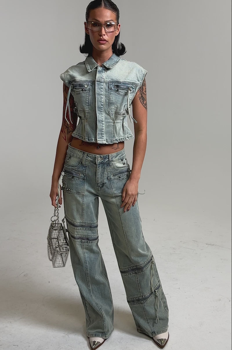 A video of a woman in the COMEBACK ERA WIDE LEG DENIM JEANS with a sleeveless light blue crop top, clear glasses, and a small geometric purse.