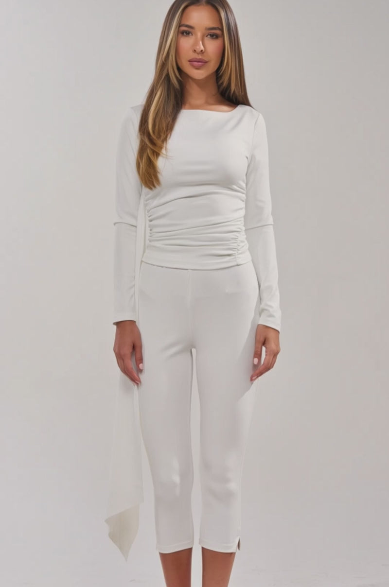 Video of woman modeling the MODEL OFF DUTY TOP, a fitted white ruched long sleeve style, paired with matching white cropped pants and clear-heeled sandals.