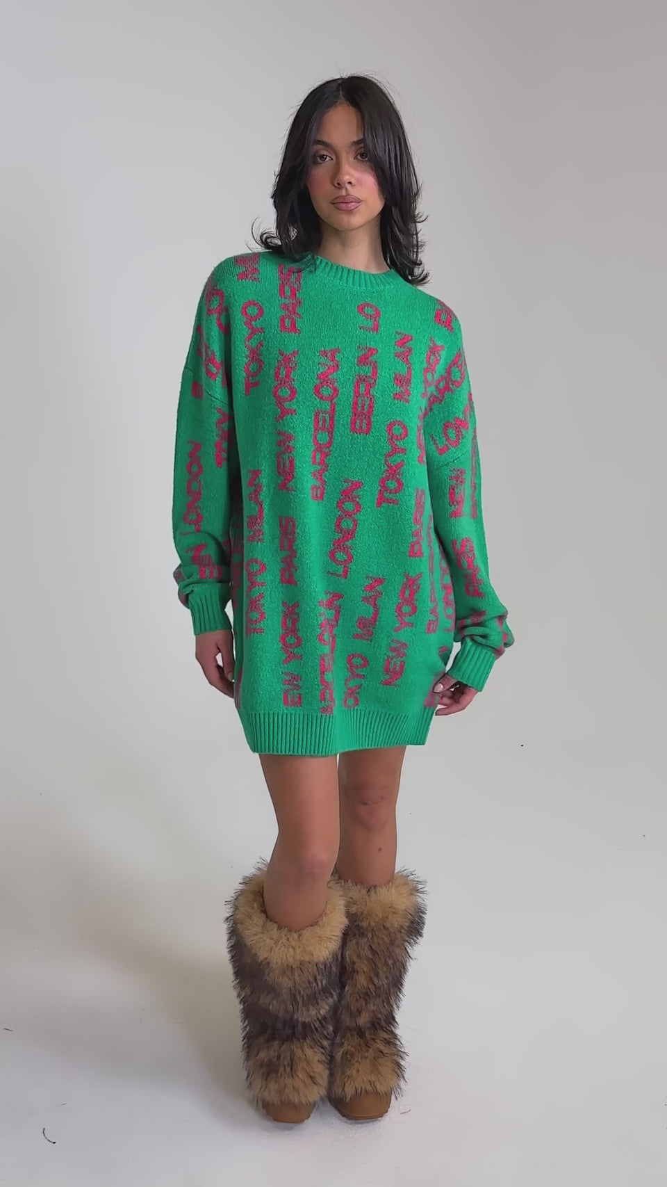A video of a woman wearing the AROUND THE WORLD SWEATER MINI DRESS IN GREEN and fluffy brown boots.