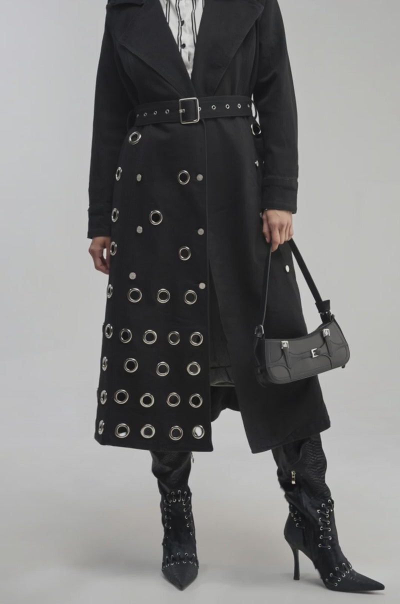 Video of a woman modeling the PHOENIX DENIM TRENCH—a black denim trench coat with silver grommets.