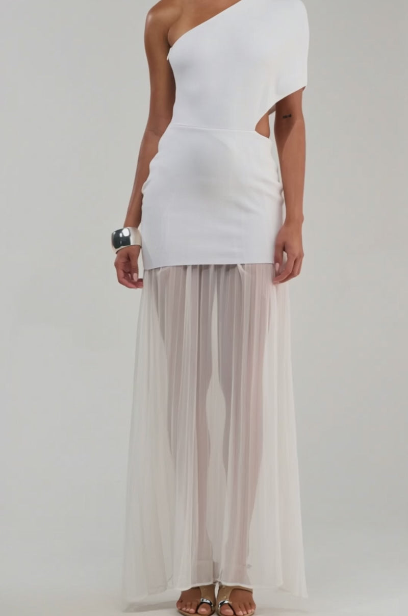 Video of woman modeling the FINAL BOW ASYMMETRICAL MAXI DRESS IN WHITE, a bridal-inspired one-shoulder style with a fitted mini skirt and sheer pleated maxi overlay, styled with silver earrings, a cuff bracelet, and strappy heels against a plain light background.