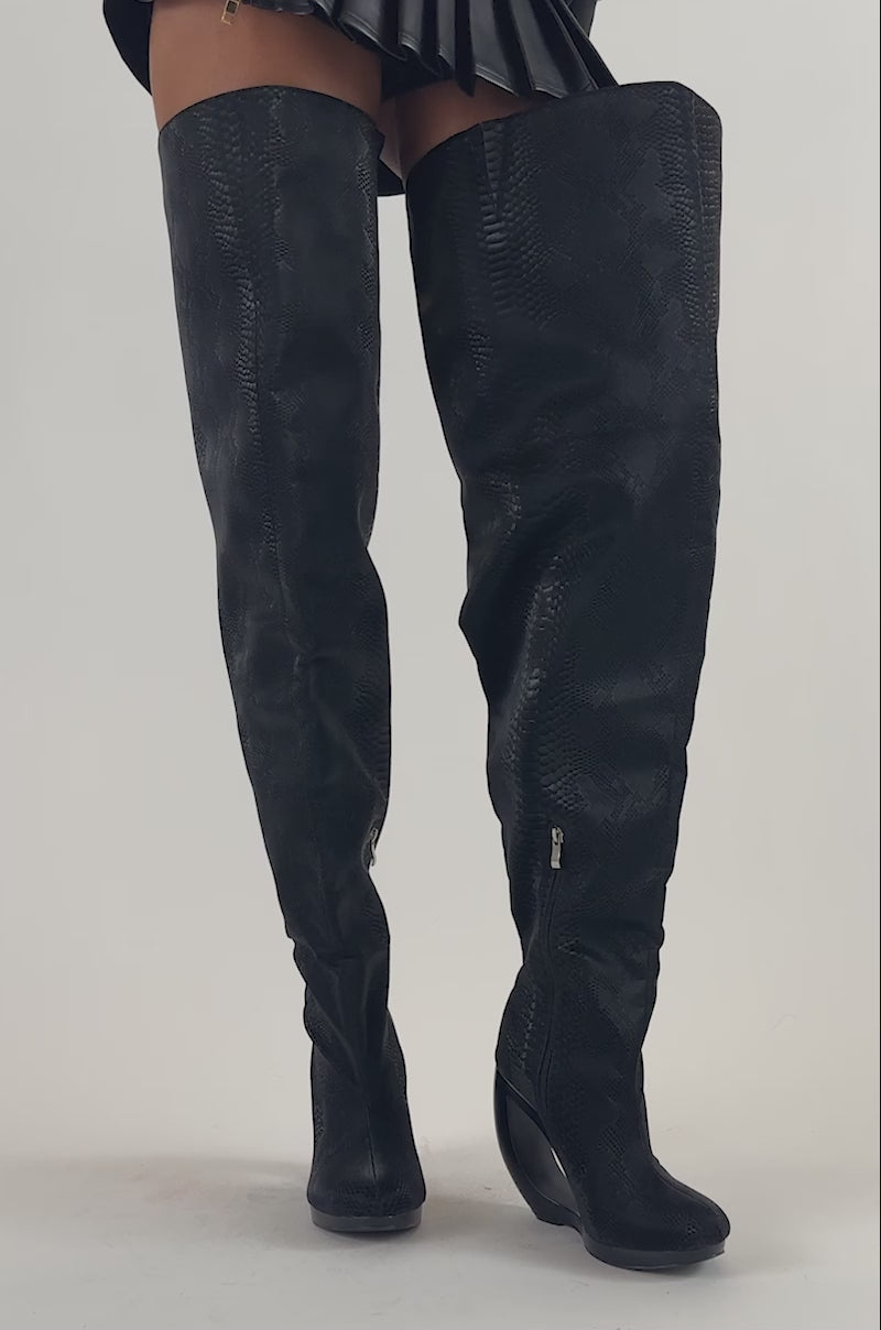 Video of a woman modeling the AZALEA WANG ASA BLACK SNAKE OPEN WEDGE THIGH HIGH BOOT, featuring striking curved heels.