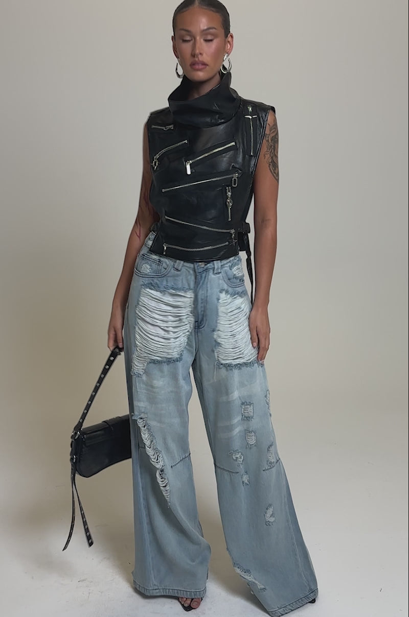 Video of woman modeling the ZIP ME UP TURTLENECK TOP IN BLACK with ripped light blue jeans, posing confidently against a plain gray background.