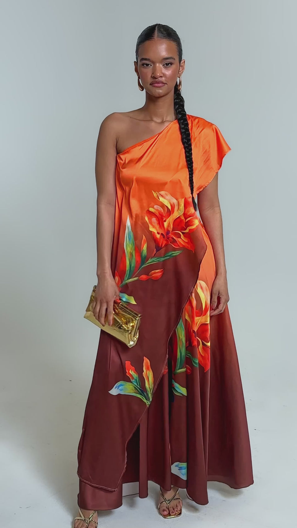 Video of woman modeling the SUNSET LOVER PALAZZO PANT, featuring a bold orange and yellow tropical floral print, paired with gold sandals and a small gold clutch. 