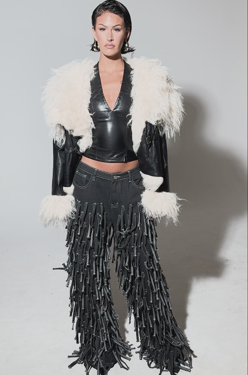 Video of woman modeling the ROSIE FUR TRIM MOTO, a black faux fur moto jacket with an oversized cream shearling collar and cuffs, paired with black tassel-trimmed pants, against a plain gray background.