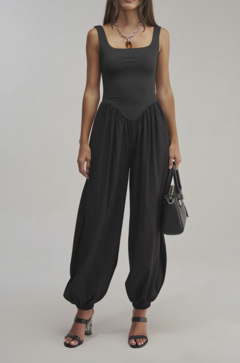 A video of a woman wearing the FLIRT ALERT SQUARE NECK JUMPSUIT and black heeled sandals, holding a black handbag.