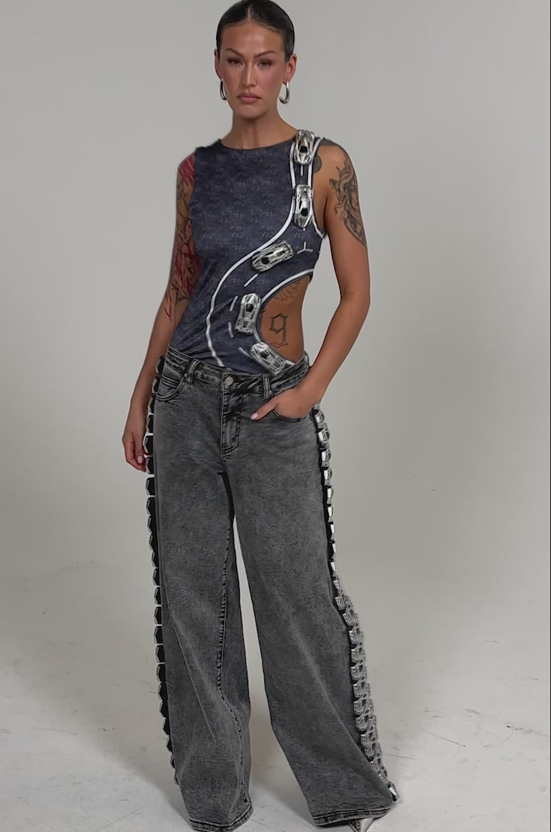 Video of woman modeling RACE CAR DENIM jeans with metallic detailing, and holding a matching handbag.