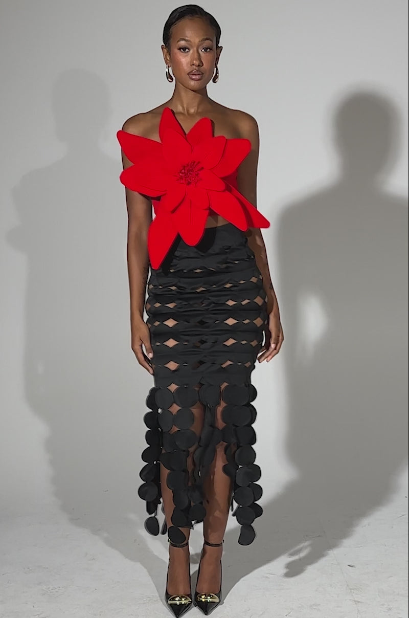 A video of a woman wearing the LOOKING FOR ME CIRCLE CUTOUT SKIRT paired with a bold flower-shaped top and metallic pointed-toe heels, standing against a plain light background.
