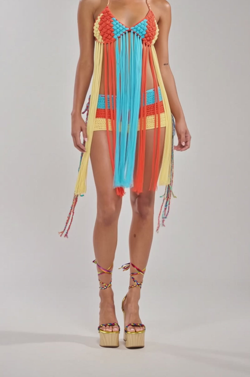 A video of a woman wearing the BEACHIN CROCHET SHORT IN ORANGE, styled with a colorful crochet dress featuring long fringe.