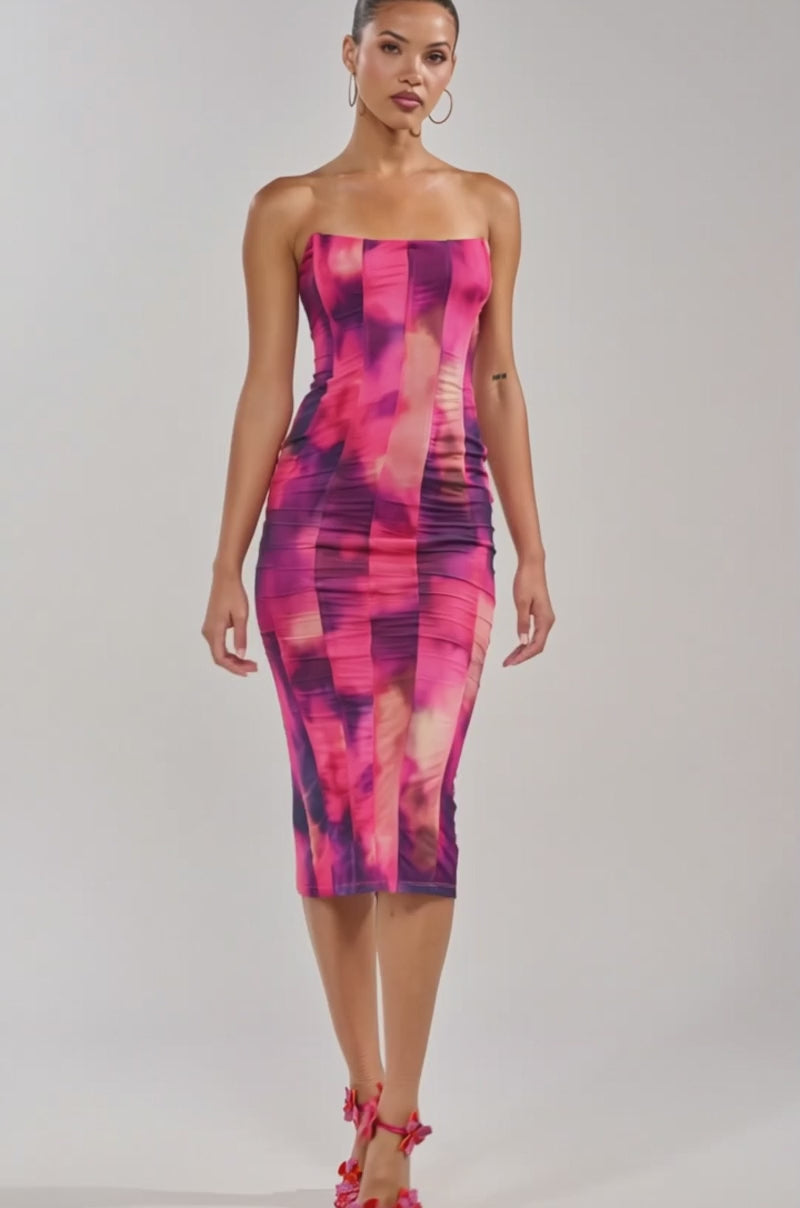 A video of a woman in the ROSE GARDEN MAXI DRESS IN PINK MULTI, a body-hugging, strapless dress with a vibrant pink and purple abstract print. 