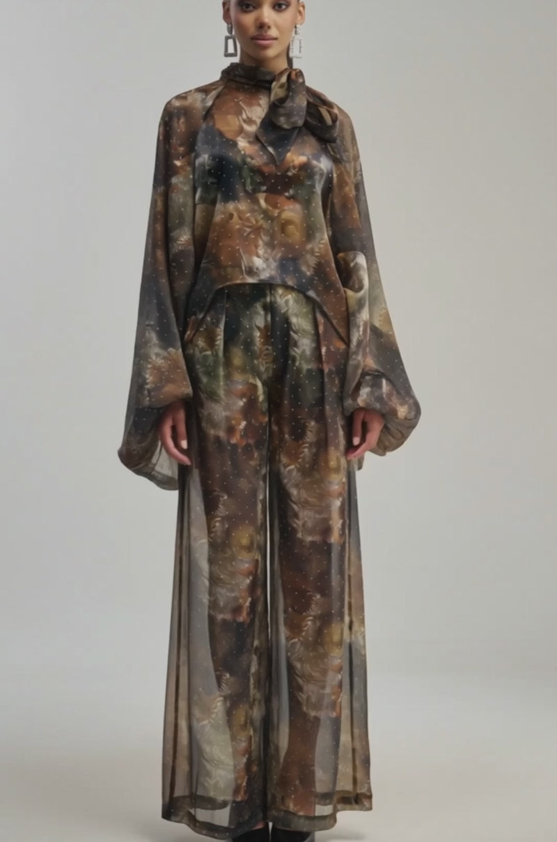 Video of a woman modeling the LADY LUXE BLOUSE—a sheer, long-sleeved brown and black patterned piece featuring a high neck and oversized bow, reminiscent of elegant balloon sleeves.