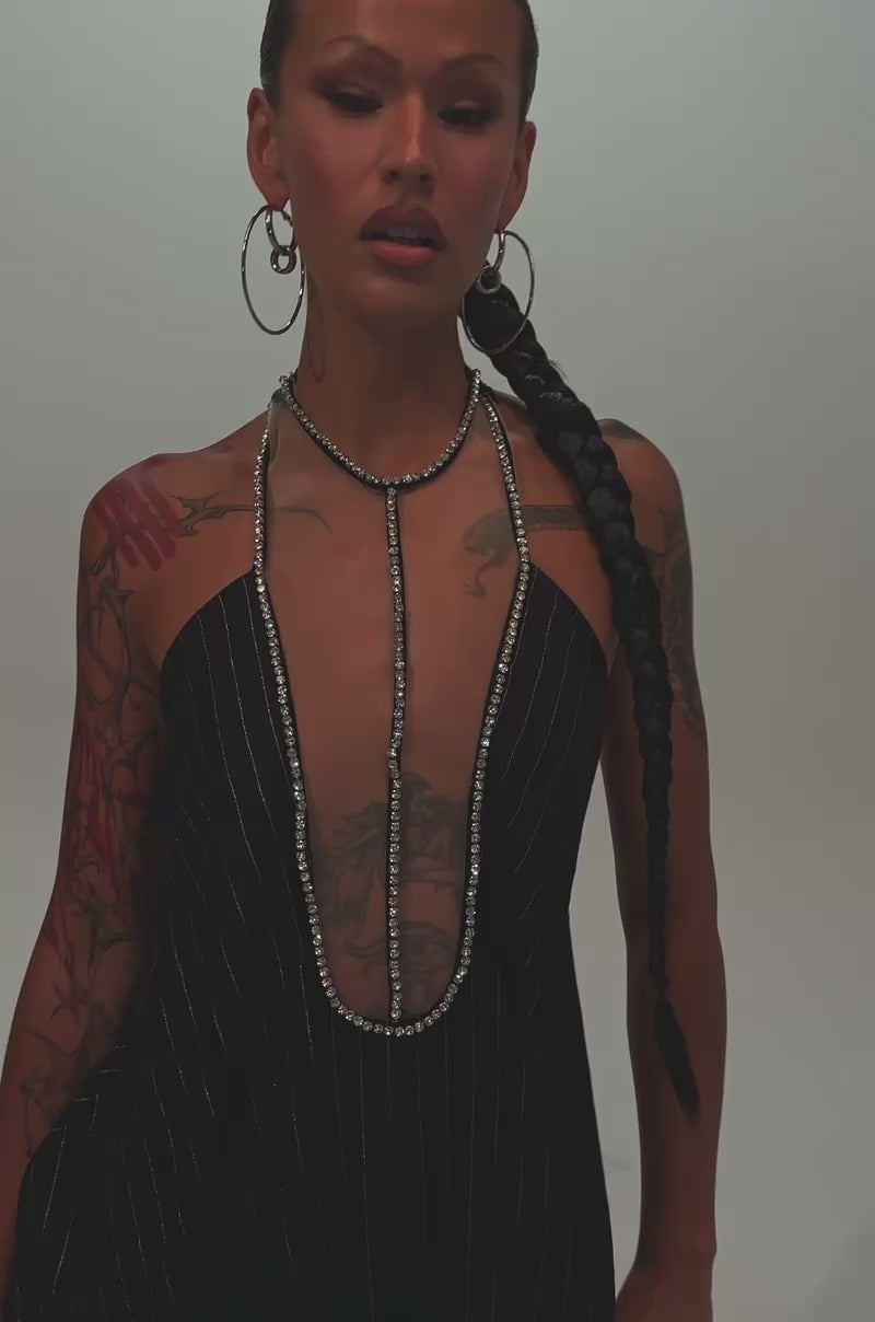 Video of a woman modeling the READY FOR BUSINESS PINSTRIPE JUMPSUIT. The loose, black pinstripe jumpsuit features a deep neckline.