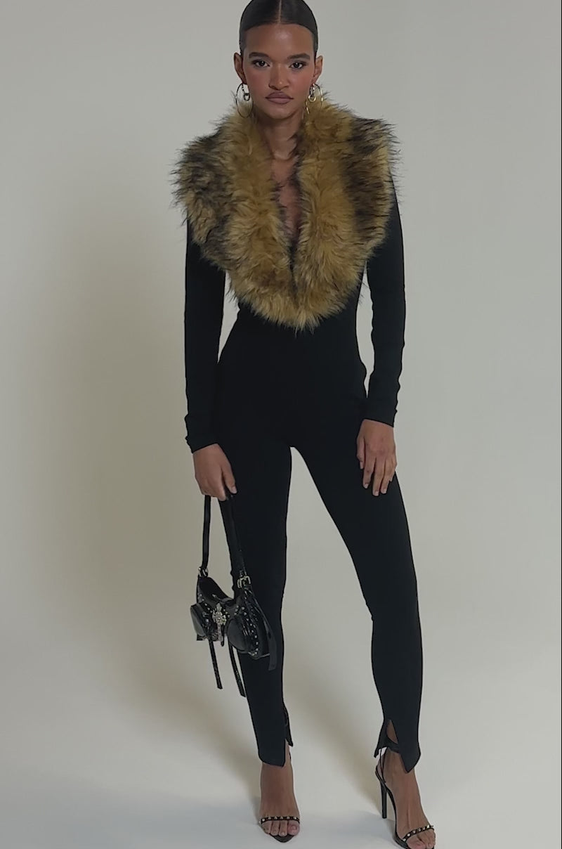 Video of woman modeling the OH HOT DAMN BABY FUR TRIM JUMPSUIT featuring a fitted silhouette and deep V neckline, accessorized with a black handbag and strappy heels—an ideal look for a luxurious night out.