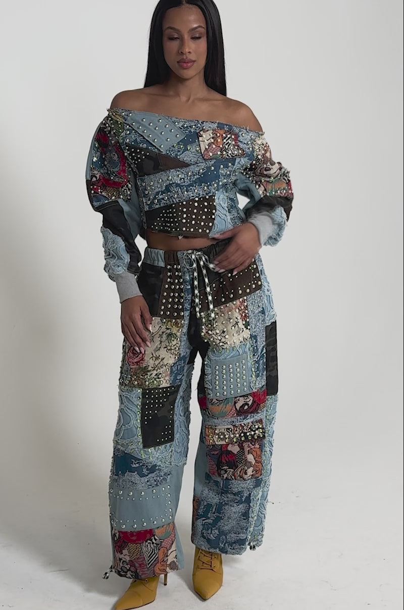 A video of a woman in the CALL ME CRAZY PATCHWORK OFF THE SHOULDER SWEATSHIRT paired with matching wide-leg pants, both featuring colorful patchwork denim and studded details.