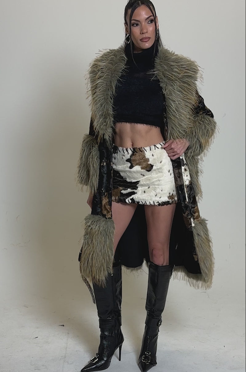 Video of woman modeling the FREYA FUR TRIM TRENCH, styled with a black belt, turtleneck, and tall black boots, stands against a plain gray background.