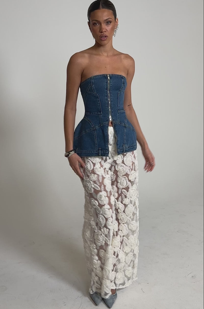 A video of a woman wearing a strapless, zip-up denim peplum top with CRYSTAL PALAZZO PANT—wide-leg pants featuring 3D floral sheer fabric and large rosette appliqué—standing against a plain background, facing forward.