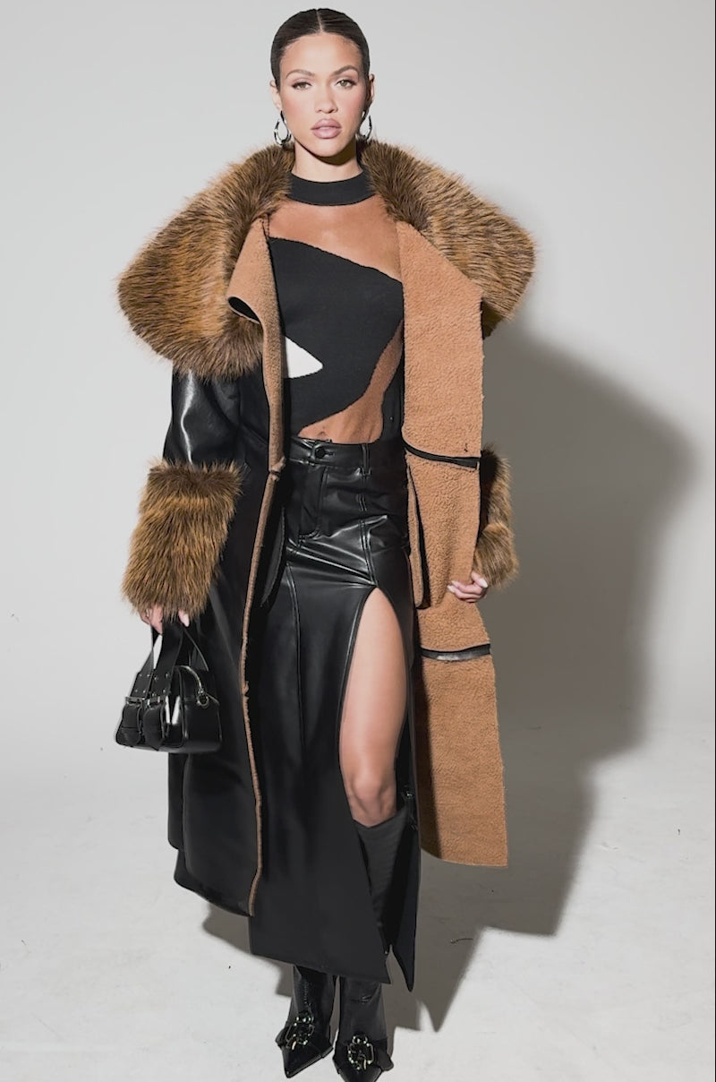 Video of a woman modeling the SIREN FUR TRIM TRENCH COAT with a large brown faux fur collar and cuffs, styled over a black top, high-slit black skirt, and knee-high boots against a plain backdrop.