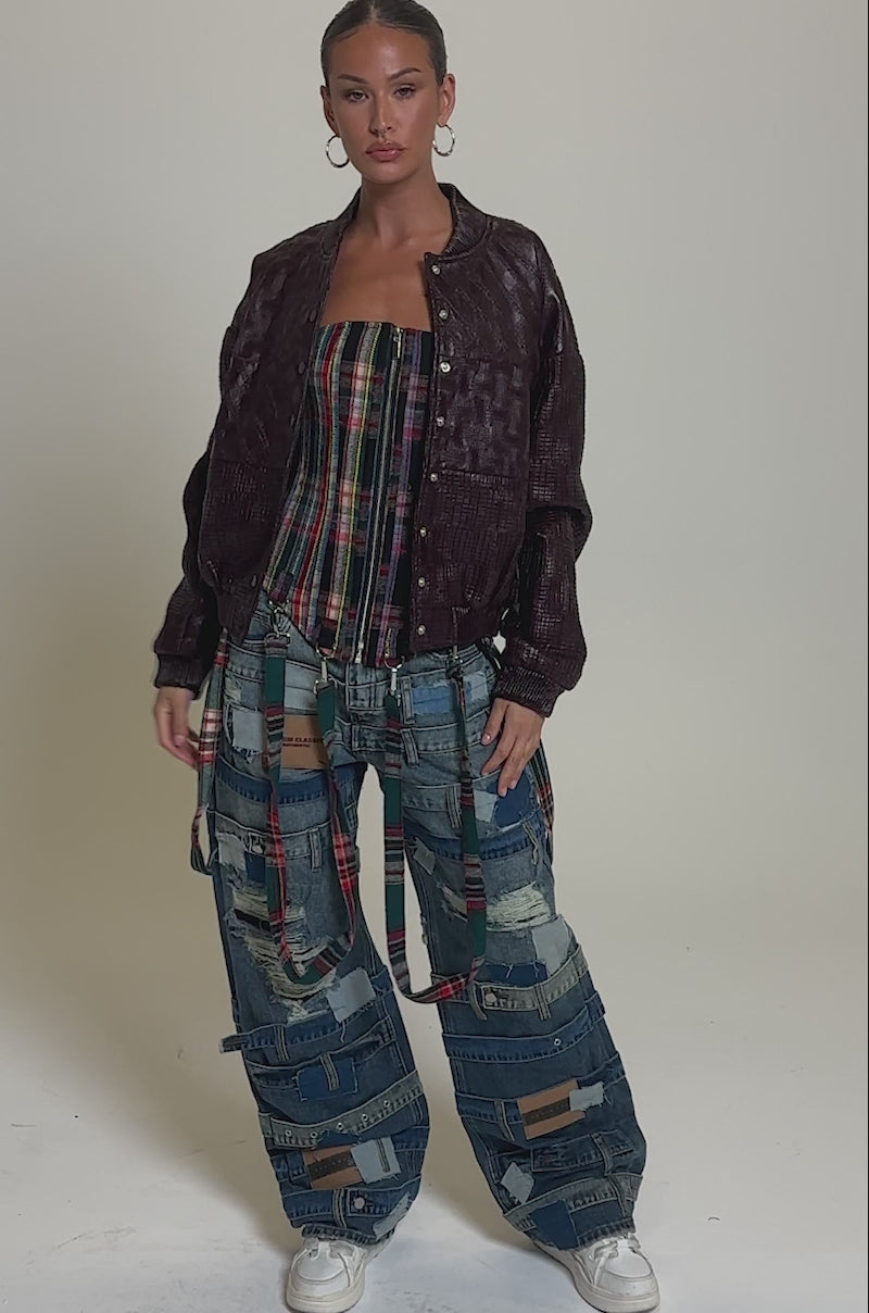 Video of woman modeling the CHARLI PATCHWORK BOMBER over a plaid top and jeans with plaid strips, her hair slicked back and accessorized with large hoop earrings.