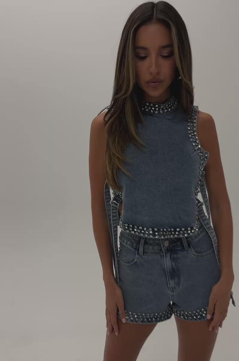 Video of woman modeling the LOVE ME RHINESTONE DENIM TOP and matching high-waisted shorts, featuring rhinestone accents and side ties—an easy, festival-ready look. 