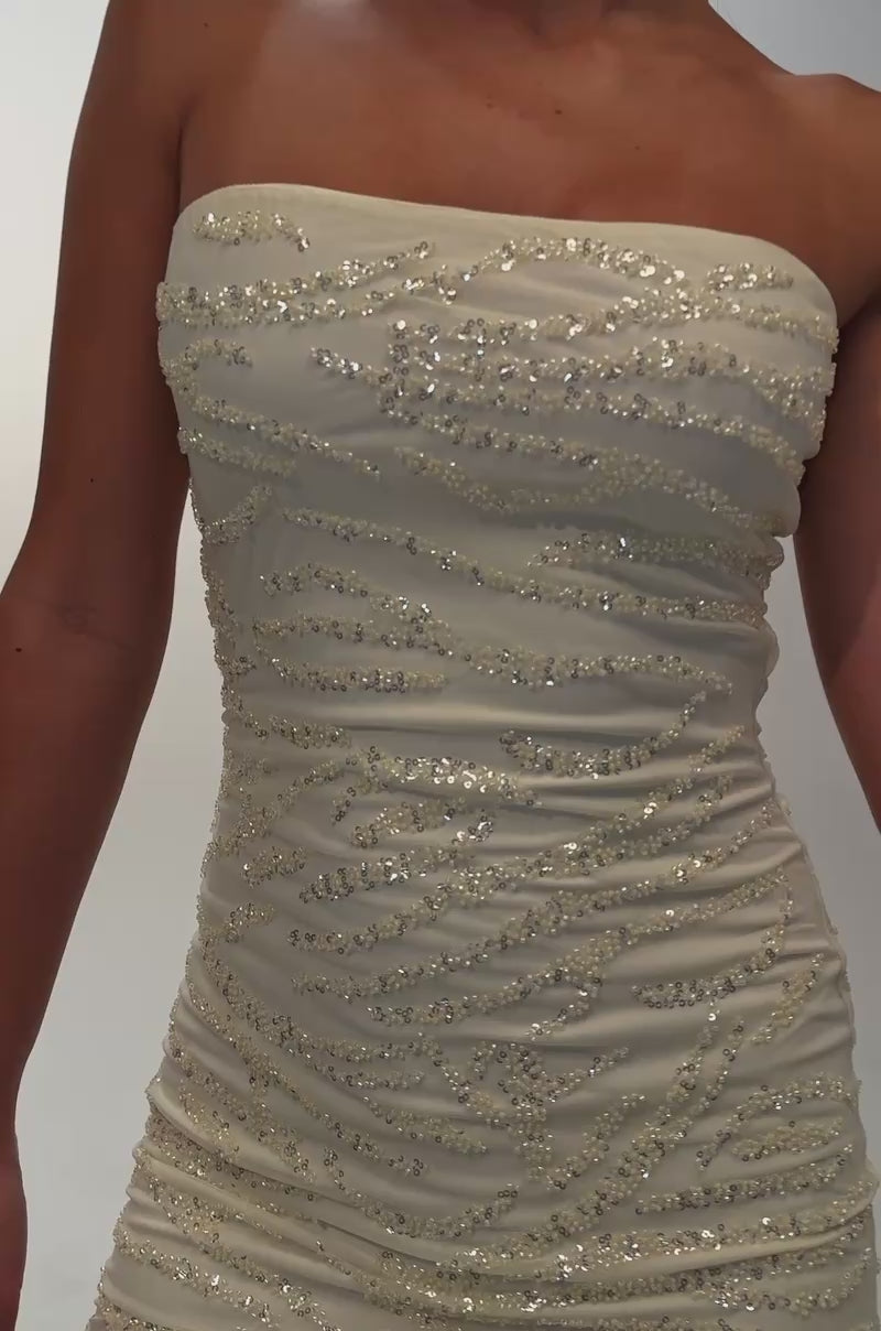A video of a woman in the CUTE AND FLIRTY SEQUIN MINI DRESS IN YELLOW—a strapless bodycon mini dress in pale yellow, adorned with textured wavy details. 
