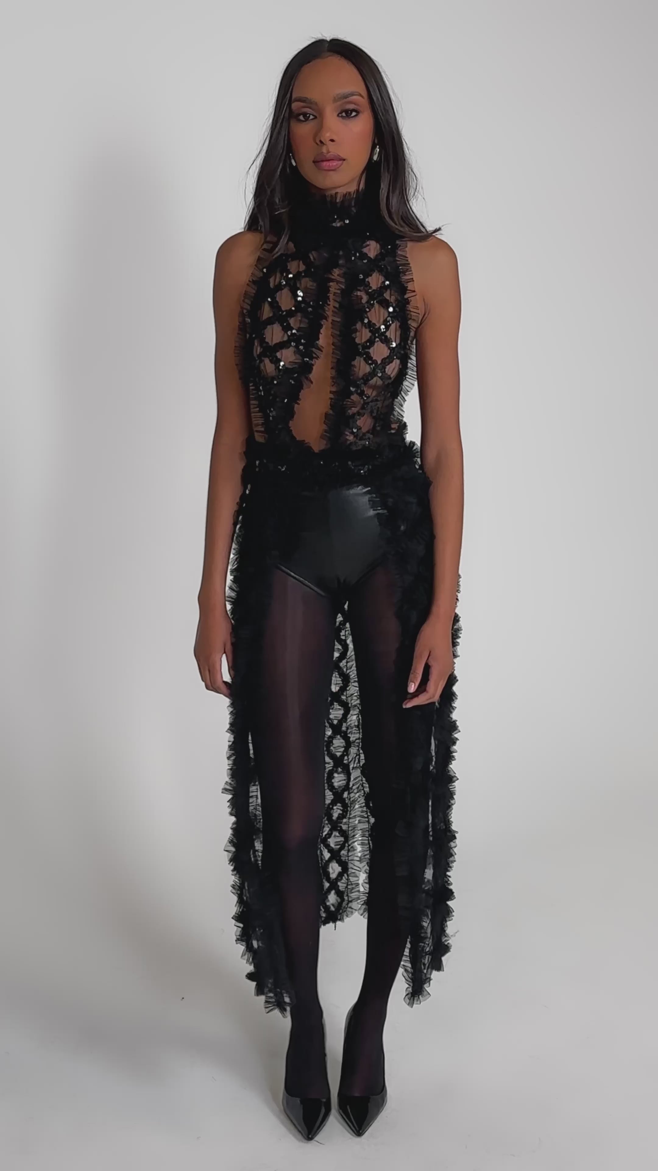 Video of woman modeling the BRING ON THE DRAMA BLOUSE—an eye-catching black, textured top with sheer panels and fringed accents, styled with black tights and high heels against a plain gray background.