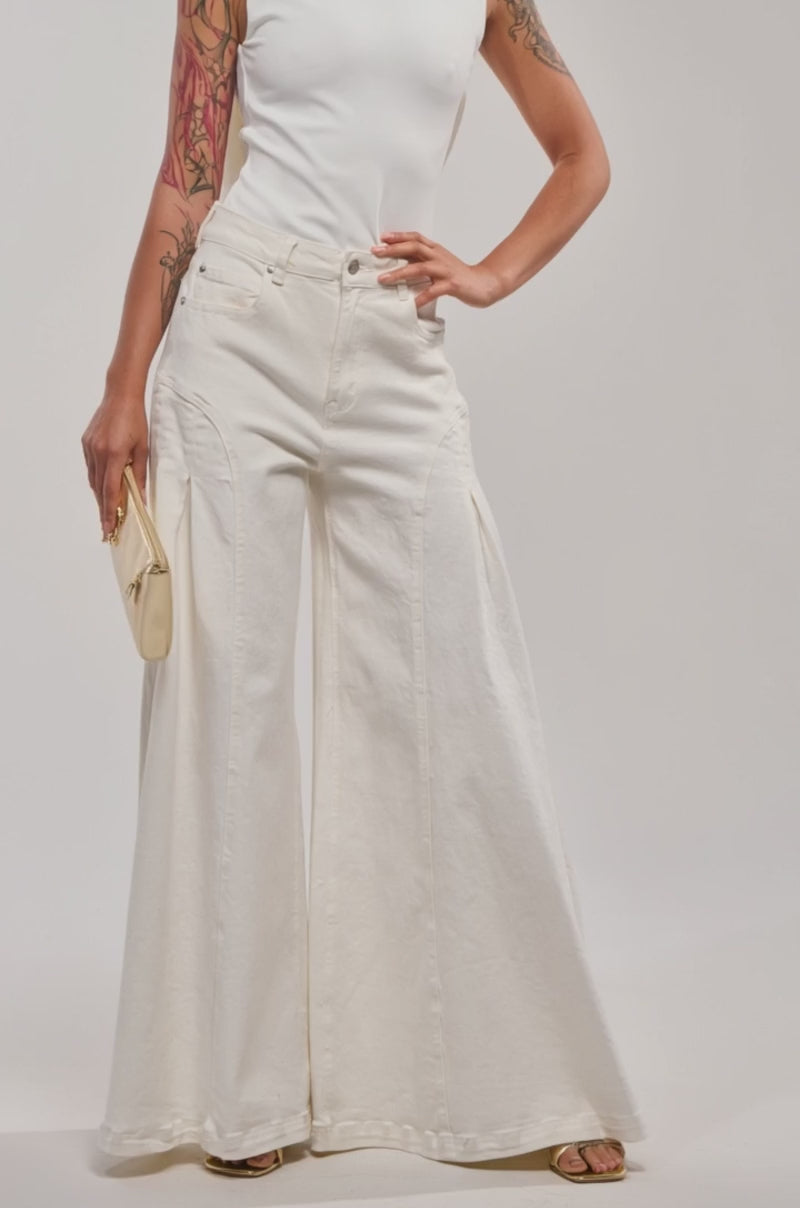 A video of a woman in the STAY CLASSY STRETCH BODYSUIT and wide-leg white jeans, holding a small gold clutch. 