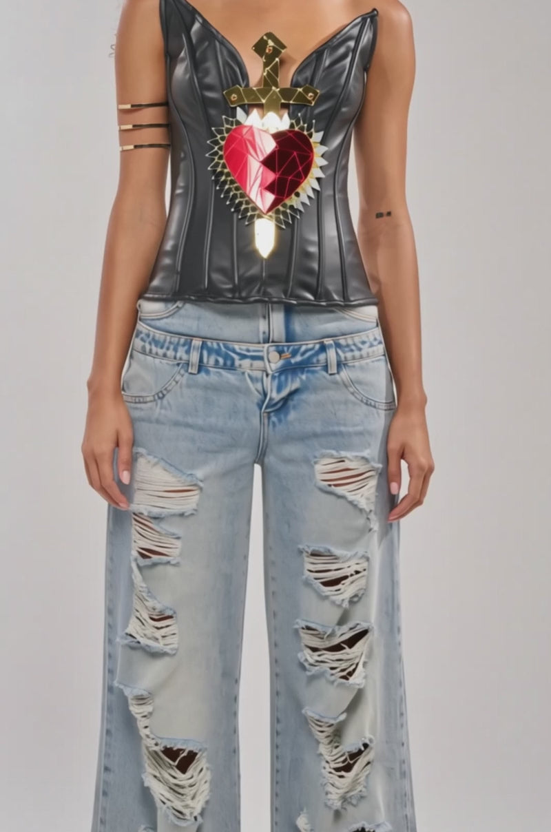 Video of woman modeling the LOVERS CLUB CORSET, a black top adorned with a gold sword and mirrored heart on the chest. She pairs it with gold hoop earrings, gold arm cuffs, denim jeans, and displays a small tattoo on her left arm.