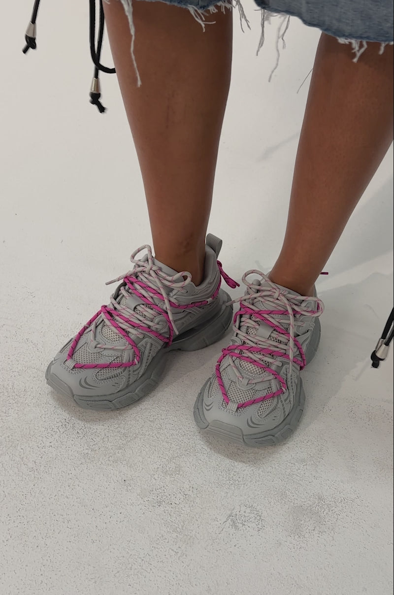 Video of woman modeling the AZALEA WANG SATINE GREY LACE UP SNEAKER with bright pink laces and a blue denim short decorated with silver studs and bold black lace-up sides, a person stands against a plain, light-colored background.