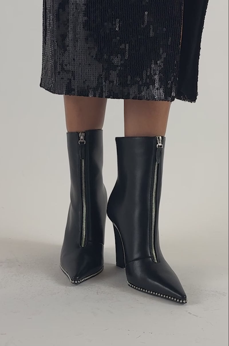 Video of a woman modeling the AZALEA WANG ROSARIO BLACK WEDGE BOOTIE WITH STUD DETAIL, featuring pointed toes, zippers, and silver studs on the soles.