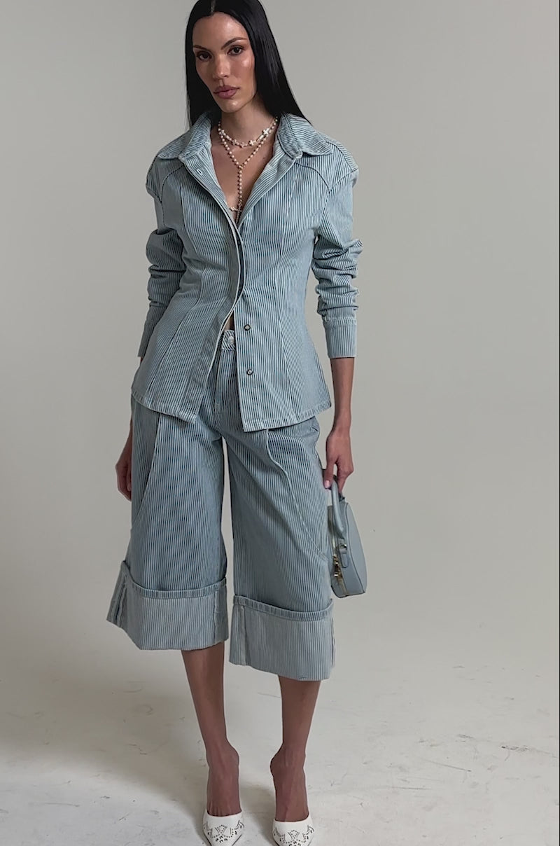 A video of a woman in the FEEL FREE STRIPE GAUCHO set—a light blue pinstriped jacket and matching wide-leg cropped pants. 