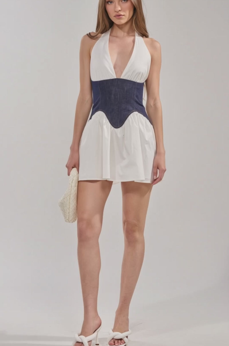 Video of woman modeling the SAY LESS Poplin Mini Dress in White—a sleeveless dress featuring a deep V-neck and a dark blue denim corset-style waist. She holds a textured white handbag, perfect for your next spring brunch look.