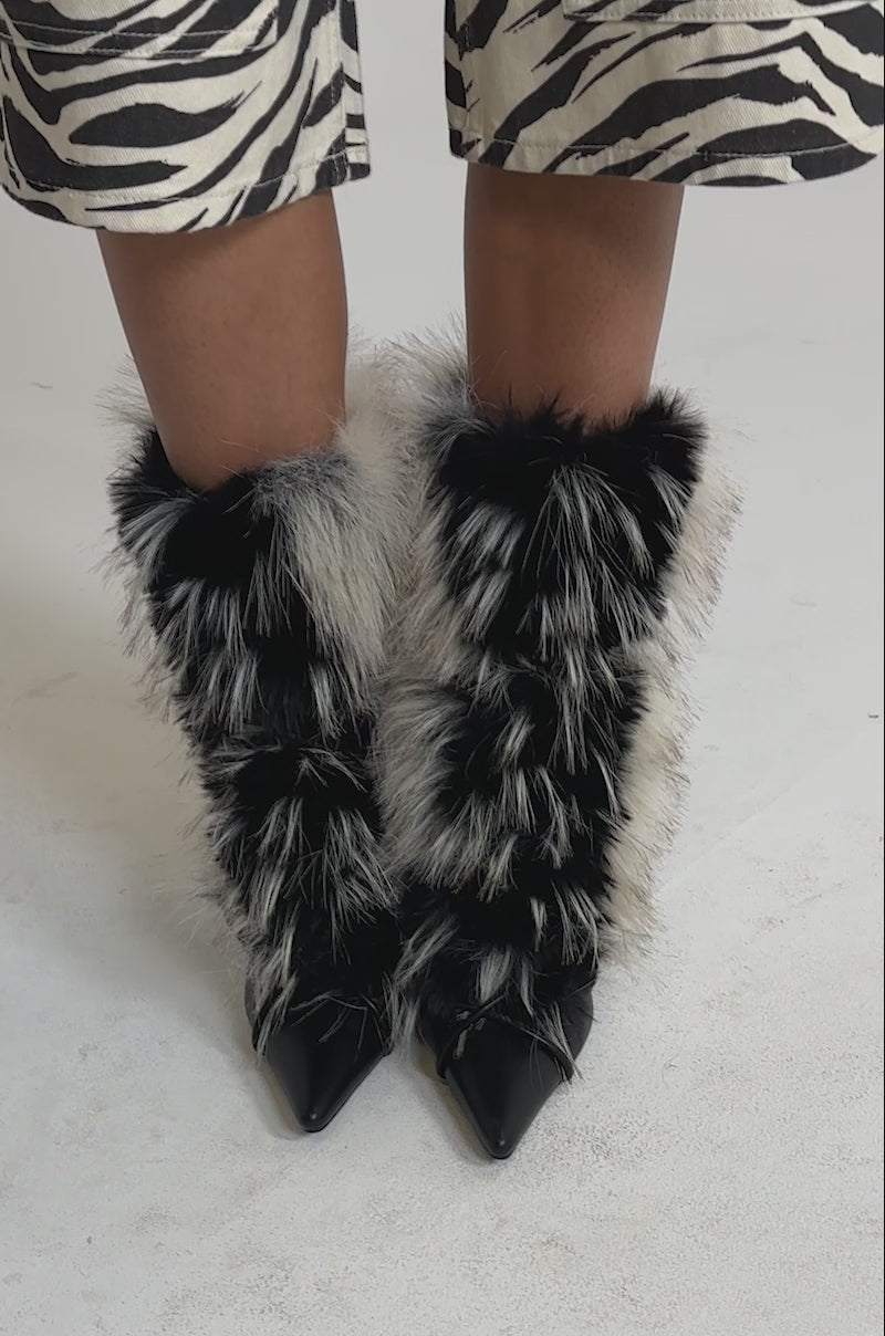A video of a model wearing a knee-length zebra print skirt and AZALEA WANG MAHTAMA BLACK AND BEIGE FUR STILETTO BOOTIE with shaggy, multicolored faux fur lining at the ankles and front.