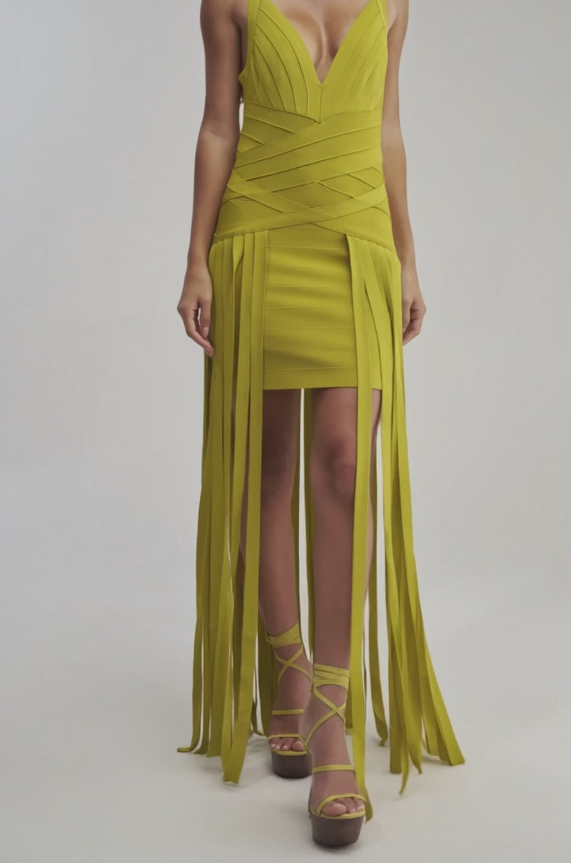 A video of a woman in the LUCKY CHARM FRINGE MINI DRESS—a sleeveless, chartreuse bandage mini dress with a deep V-neck, long vertical fringe accents, and gold platform heels.