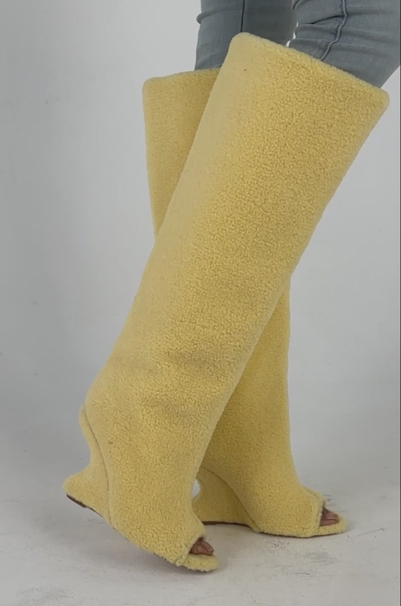 Video of a woman modeling the AKIRA GOLD VINCENT SHERPA CREAM OPEN TOE WEDGE BOOT—tall, fuzzy sherpa wedge boots featuring a comfort cushion insole. 