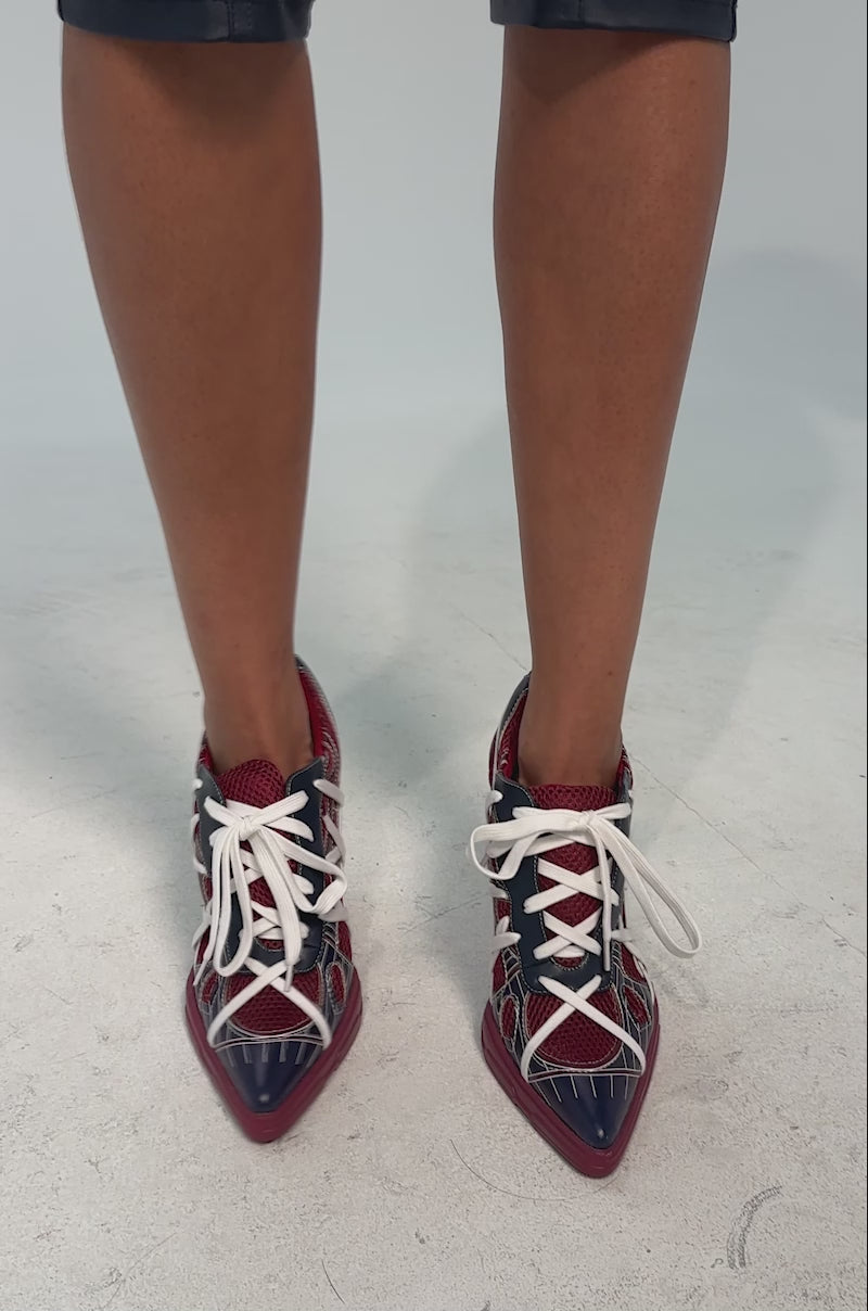 A video of a model wearing the AZALEA WANG CROSS WALK BURGUNDY STILETTO SNEAKER HEEL featuring a pointed toe, red mesh base, navy and red leather overlays, white crisscross straps, and white laces.