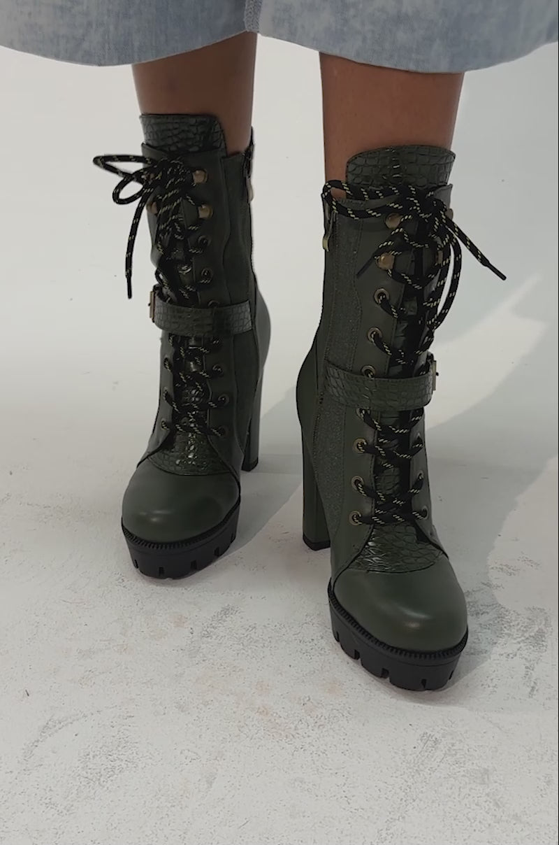 Video of a woman modeling the AZALEA WANG BARREL GREEN PU LUG SOLE BOOTIE—green platform block heel combat booties featuring chunky soles, gold zipper, and buckle details.