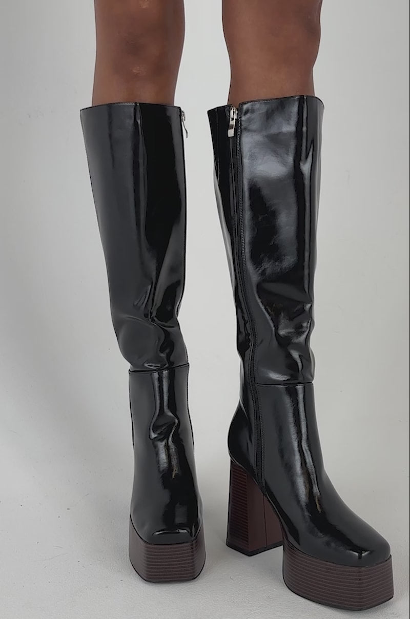 Video of a woman modeling the AZALEA WANG AUGUSTINE BLOCK HEEL BOOT IN BLACK—glossy faux leather knee-high boots with chunky high heels and side zippers.