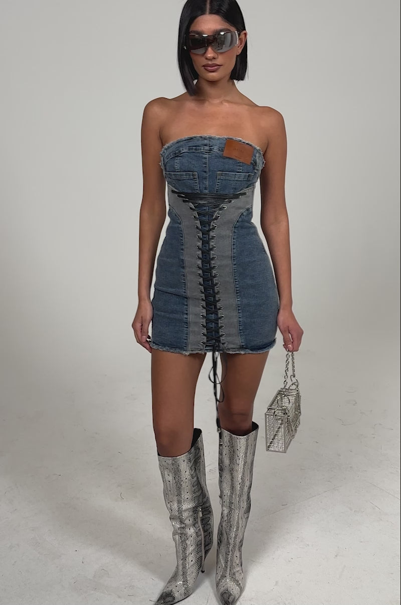 Video of woman modeling the LACED UP MINI DENIM DRESS, silver snakeskin knee-high boots, oversized sunglasses, and holding a small metallic handbag.