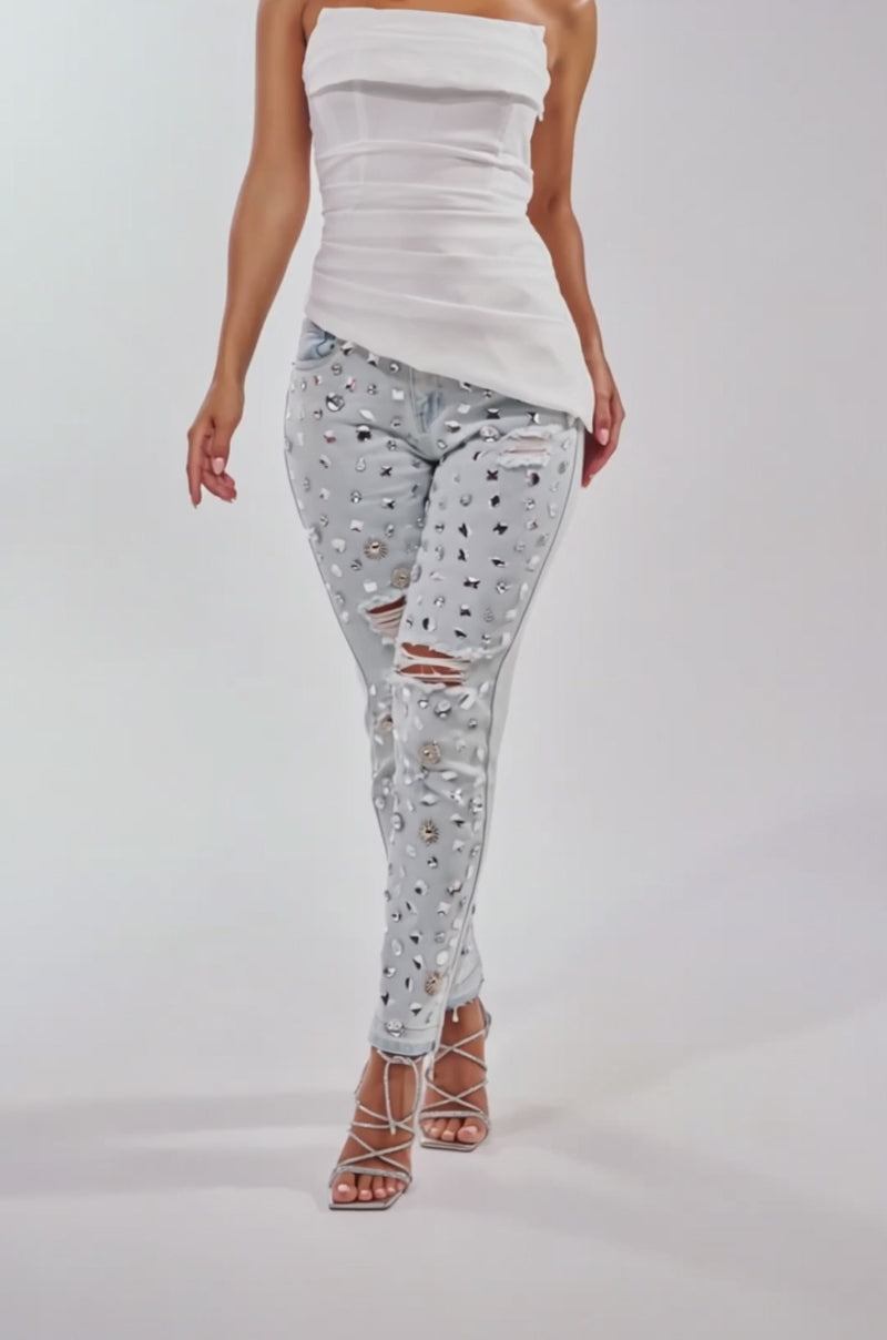 A video of a woman in a strapless white top, DAMN GIRL EMBELLISHED SKINNY DENIM in light blue, strappy silver heels, and silver jewelry against a plain white background.
