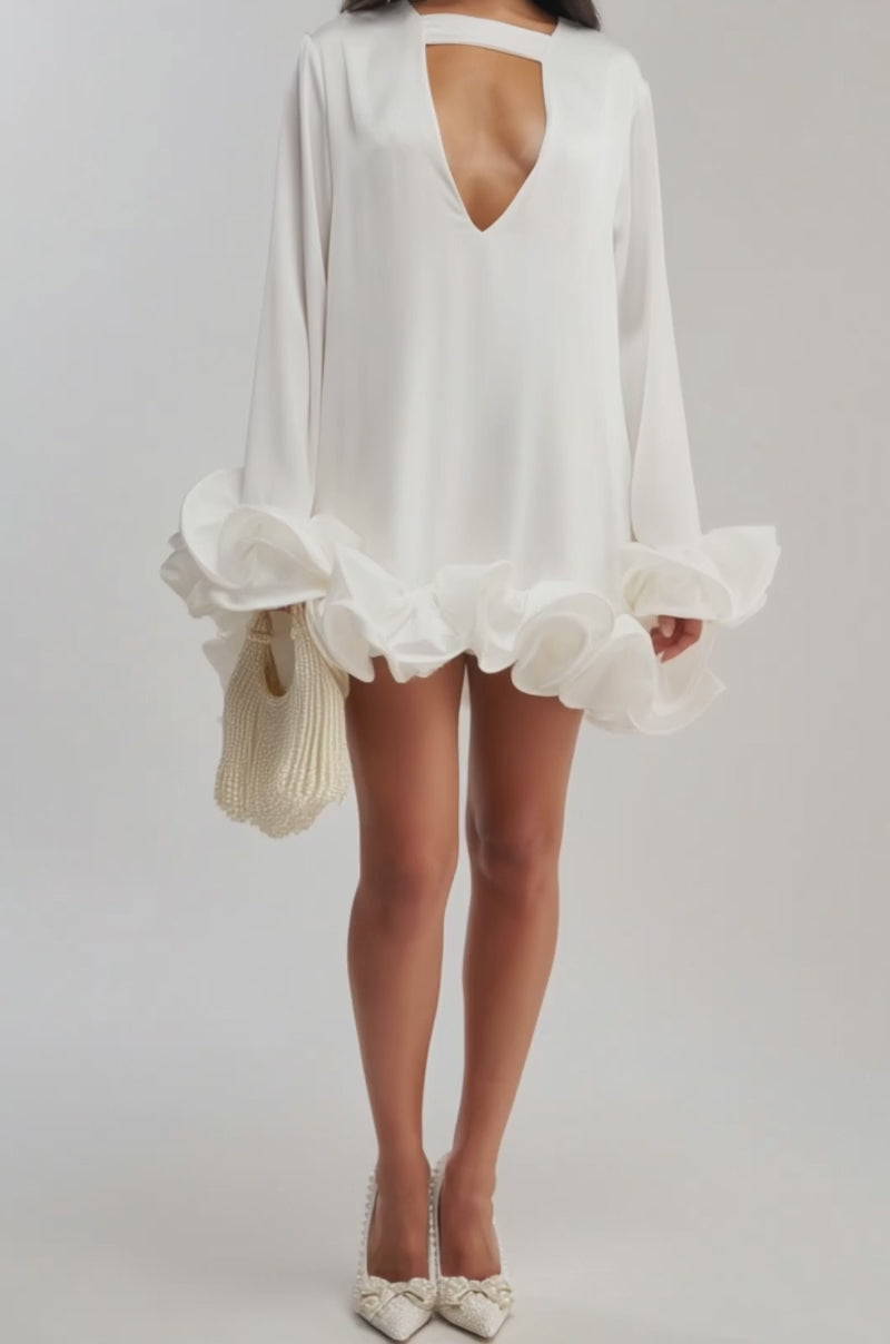 Video of woman modeling the GIRLY GIRL SATIN MINI DRESS IN WHITE, a loose mini dress with a deep V-neck, choker collar, and large ruffled hem. She completes the look with long dark hair and a pearl-adorned beaded handbag.