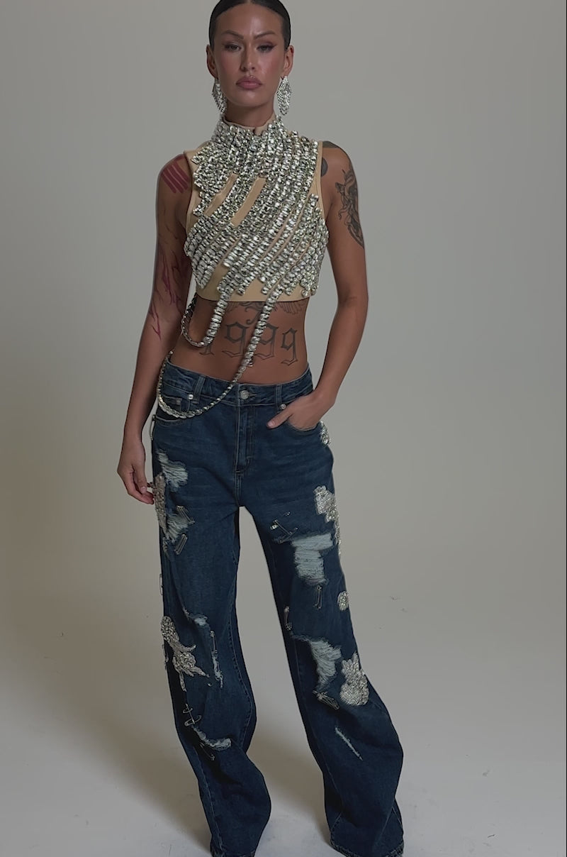 A video of a woman in the ITS YOUR TIME RHINESTONE MOCK NECK BLOUSE and wide-leg, distressed blue jeans with pearl embellishments, channeling AKIRA Label style against a plain background.