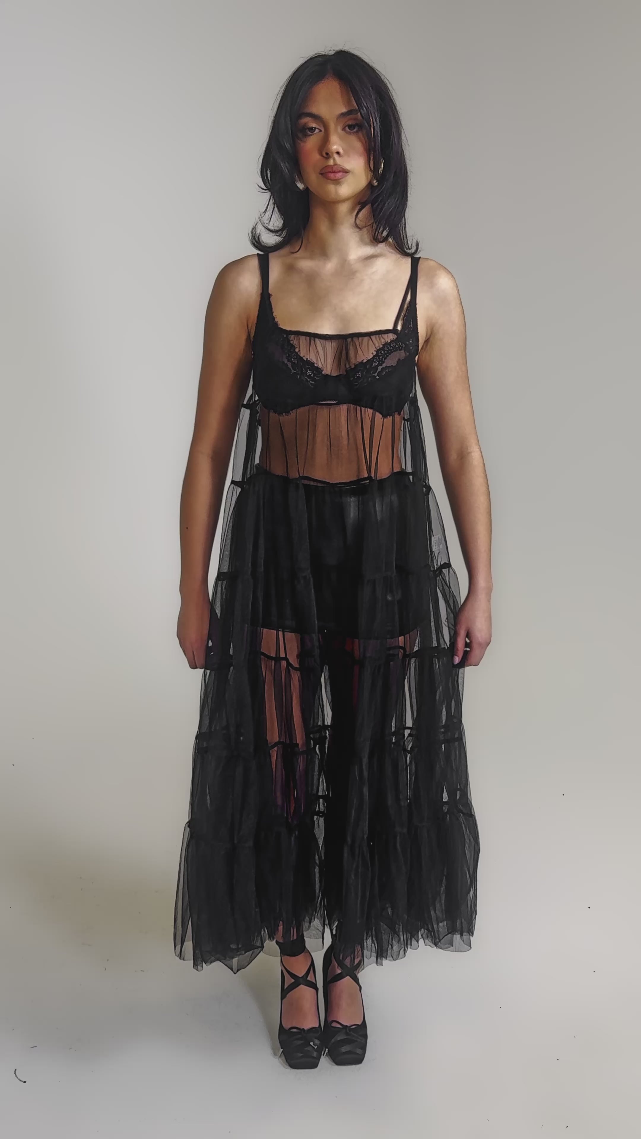 A video of a woman in the PERFECT FOR LAYERING TULLE MAXI DRESS, styled over black shorts and a matching bralette with black strappy heels.