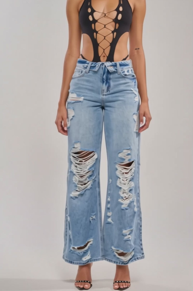 Video of woman modeling the HOTTIE BODYSUIT featuring a halter neckline with crisscross laces, plus high-waisted ripped blue jeans—posing against a light background for a stylish festival look.