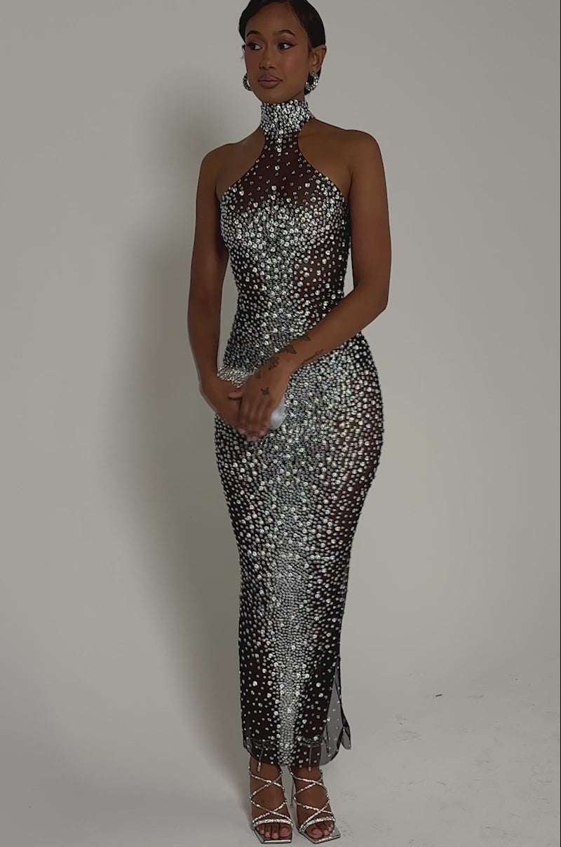 Video of woman modeling the CRYSTAL CORE MAXI DRESS, a sparkling rhinestone-embellished bodycon maxi. She holds a silver clutch, wears strappy heels, has slicked-back hair, and keeps her jewelry minimal.