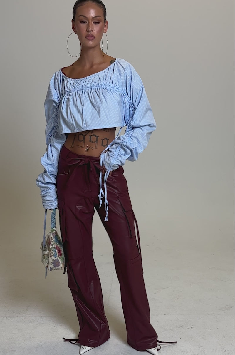 A video of a model wearing the DO SOMETHING CRAZY CARGO TROUSER with a long, a light blue crop top, and a small handbag.