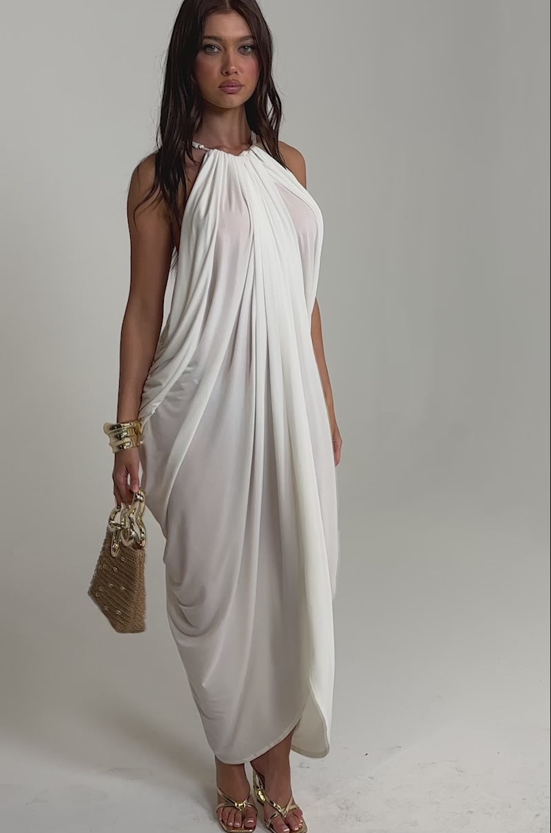 Video of woman modeling the BALI MAMI LOW BACK MAXI DRESS IN WHITE with thin straps, paired with gold block-heeled sandals and a small purse.