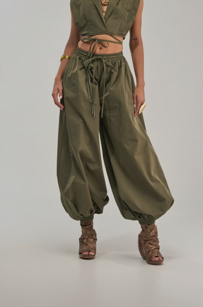 A video of a woman wearing the GUESS WHO BALLOON PANT IN OLIVE paired with a green crop top, and gold jewelry for an effortless utility-chic look.