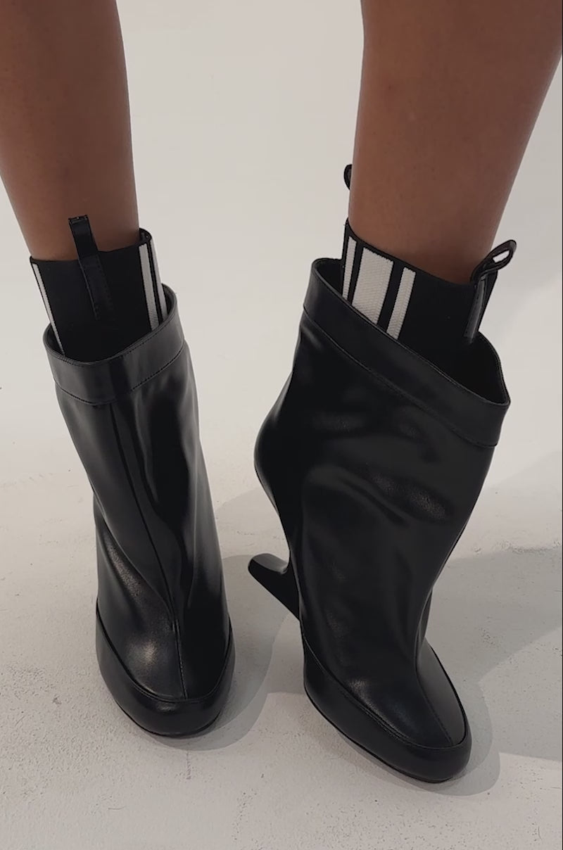 Video of a woman modeling the AKIRA GOLD ZAVI BLACK WEDGE BOOTIE.